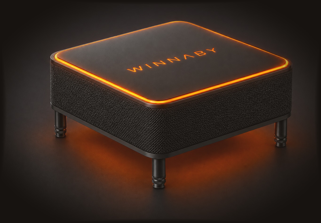 Winnaby: a small square speaker with a dark fabric body on four short legs, a soft-touch top plate with the name on it, and a glowing orange ring around the edge of the top.
